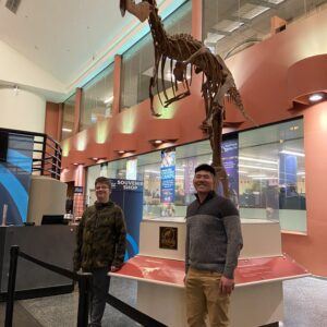 A match at a museum in front of display of dinosaur.